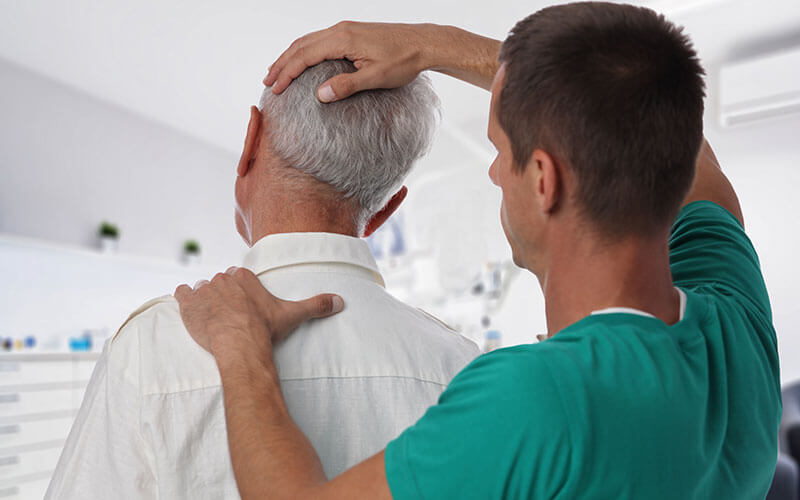 Doctor in teal scrubs provides chiropractic adjustment to senior man's neck
